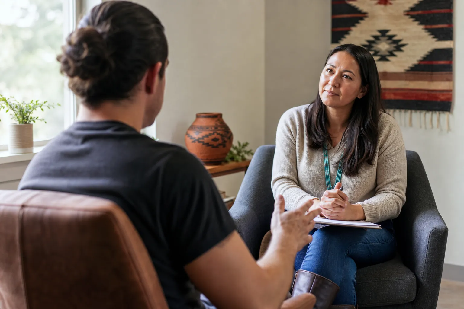 A counselor listens attentively with a notebook as a client gestures during a private addiction counseling session.