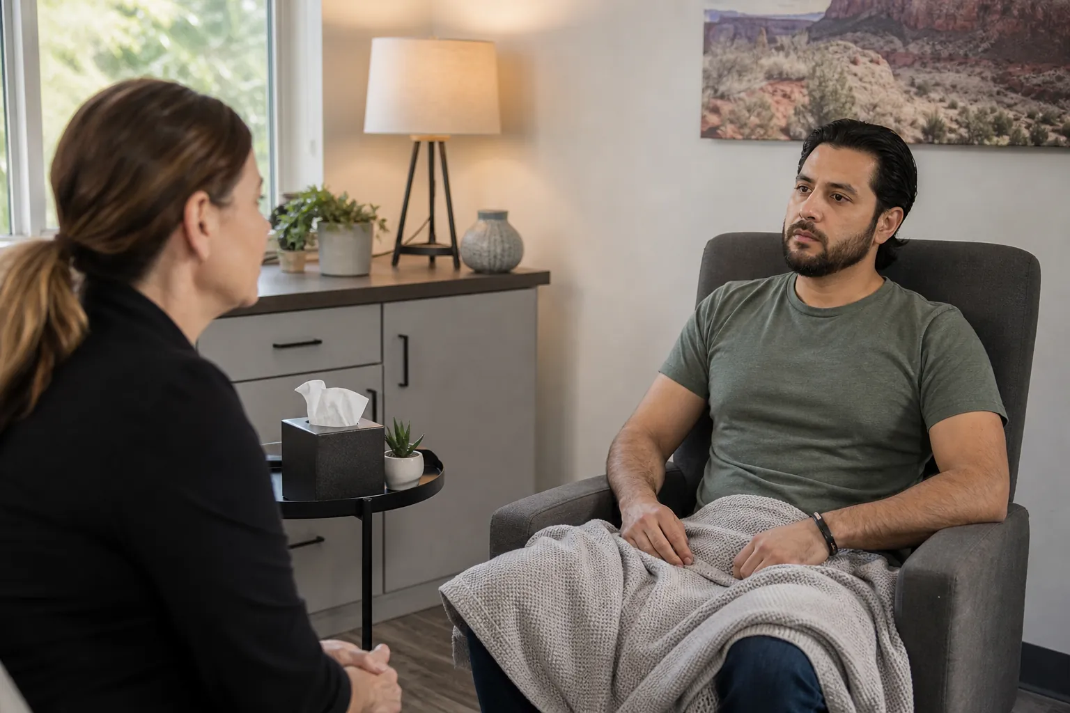 A counselor speaks with a seated man wrapped in a blanket in a calm clinical office during withdrawal treatment.