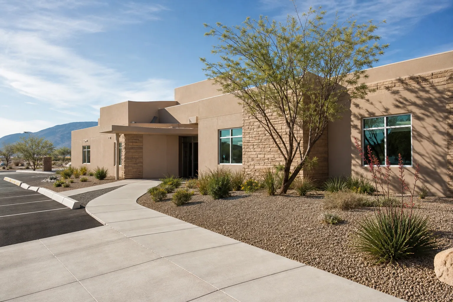 Southwestern-style outpatient facility with a curved walkway, desert landscaping, parking lot, and mountains beyond