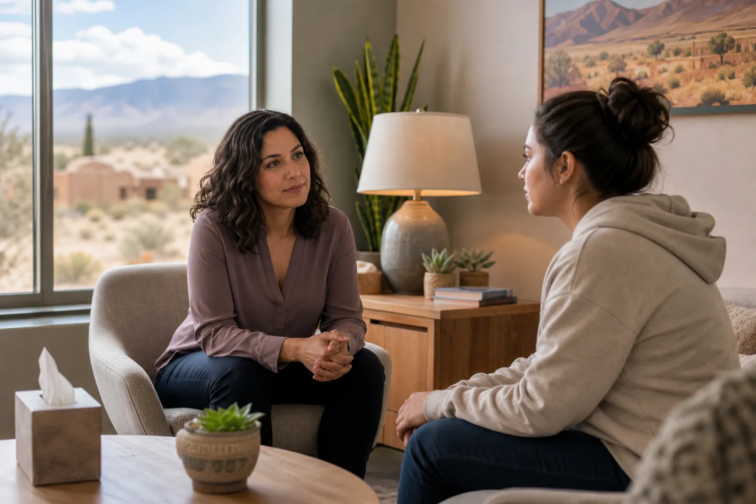 A counselor listens to a woman during a one-on-one discussion in a comfortable office with a desert view.