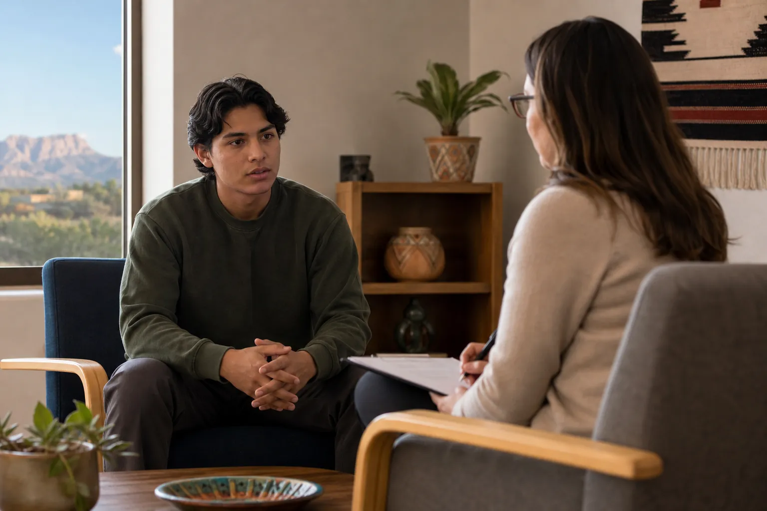 A young man speaks with a clinician holding a clipboard in an office overlooking a New Mexico desert landscape.